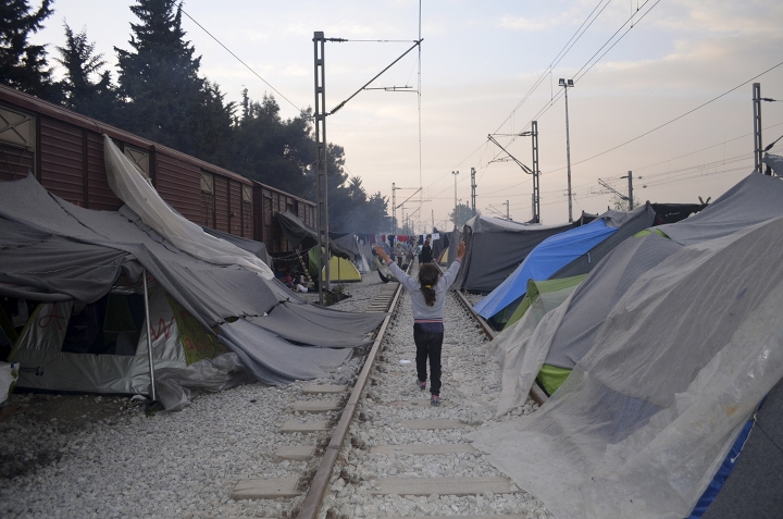 Ni&ntilde;as corren en medio del campo de Idomeni, que estaba compuesto por una antigua estaci&oacute;n de tren con antiguos ra&iacute;les y vagones (2016)