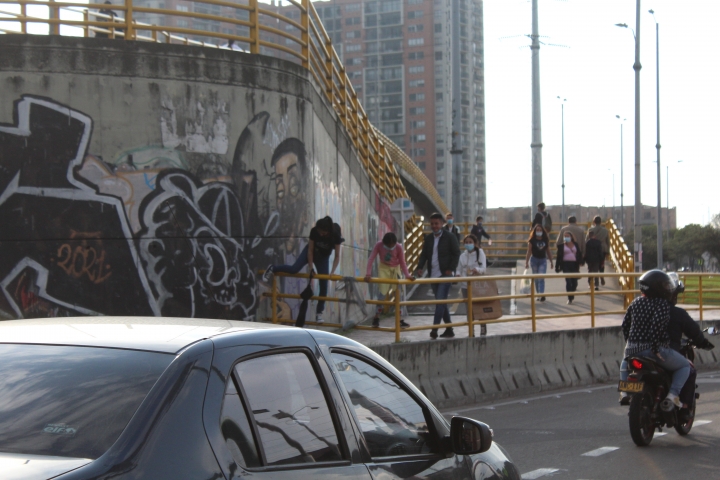 Familia con dos menores escala por la baranda del puente mientras carios vehículos se movilizan a su lado.