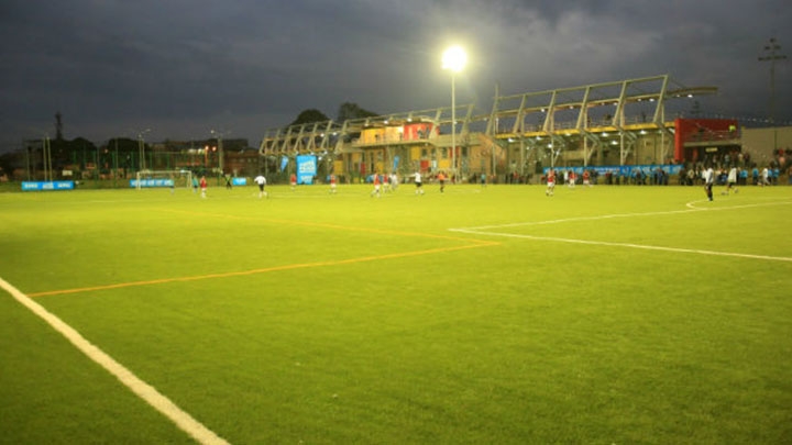 La cancha esta iluminada y tiene grama sintética