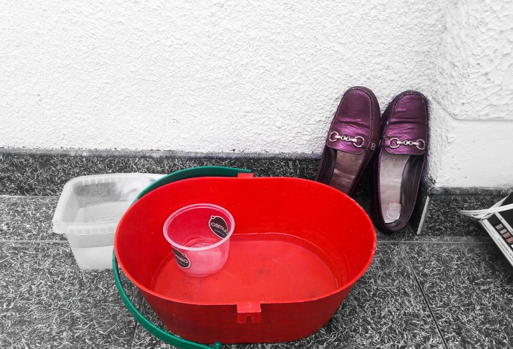 Balde con agua y jabón junto a zapatos que son usados a la hora de salir de casa para evitar la transmisión del virus