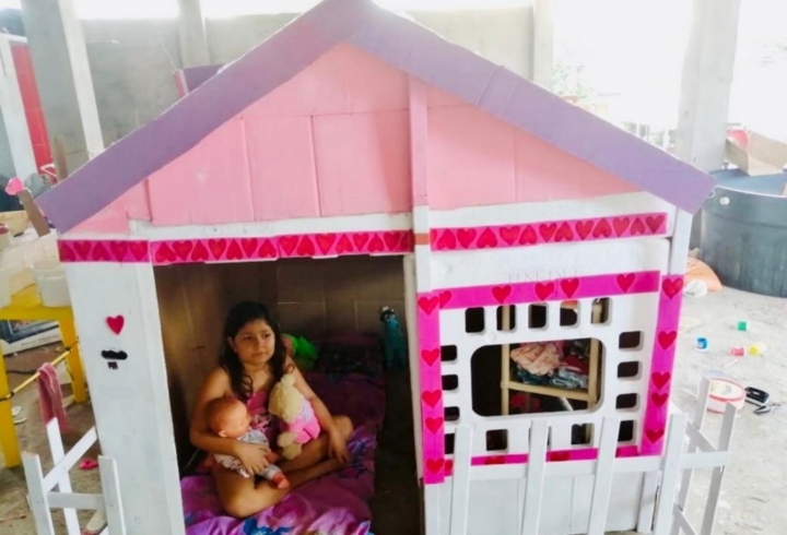 Emily juega en la casa de cartón que les hizo a sus muñecas, en compañía de su madre.